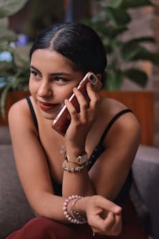 Young woman smiling while using a smartphone indoors, showcasing modern lifestyle.